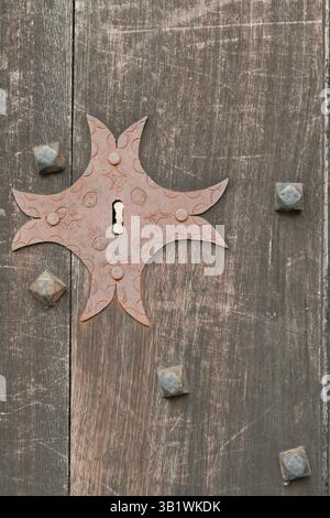 Antica croce decorativa in metallo montata su una porta di legno intemprata in un tradizionale edificio mediterraneo. Foto Stock