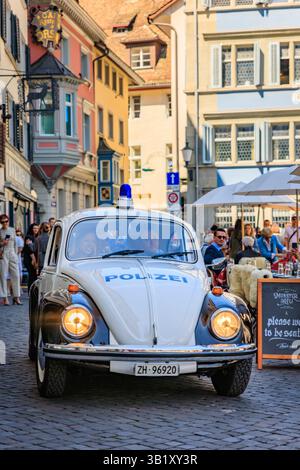 Zurigo, Svizzera - 12 aprile 2025: Iconica auto della polizia d'epoca blu e bianca con luce blu che attraversa una strada acciottolata, la città vecchia di Altstadt Foto Stock
