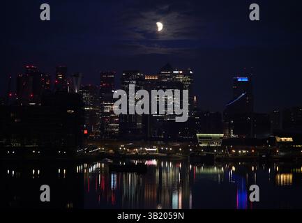 Foto datata 14/03/25 di un'eclissi lunare sopra Canary Wharf a Londra. Le banche britanniche sono destinate a rassicurare i clienti e le imprese del loro sostegno, poiché le tariffe indicano un momento di "svolta” per l'economia, dicono gli esperti. Data di pubblicazione: Domenica 27 aprile 2025. Foto Stock