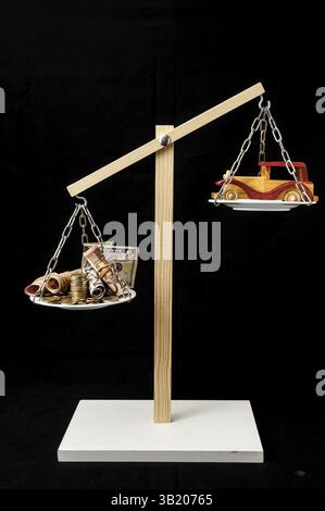 Soldi e giocattolo auto di legno su un equilibrio di due padelle Foto Stock