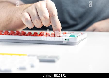 Primo piano di una persona che installa un tasto su una tastiera meccanica con interruttori rossi, sottolineando la personalizzazione pratica, la configurazione ergonomica e personale Foto Stock
