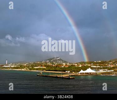 28 gennaio 2010 - Willemstad, Curacao, Antille olandesi - Un arcobaleno attraversa il cielo sopra la sezione di Otrobanda della città di Willemstad, patrimonio dell'umanità dell'UNESCO. In primo piano si trova l'architettura tendata del terminal delle navi da crociera Mega Port all'aperto sui Caraibi. Sullo sfondo c'è Zwarte Berg (Black Mountain). All'estrema sinistra sono presenti cisterne di controversa raffineria di Isla, gestita dalla compagnia petrolifera statale venezuelana PDVSA, sotto un contratto di locazione dal governo dell'isola. Cura ao è la più grande e popolosa delle tre isole ABC (Aruba, Bonaire e cura ao) delle piccole Antille. (Immagine di credito: © Foto Stock
