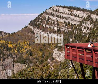 17 ottobre 2010 - Albuquerque, New Mexico, Stati Uniti - Un turista sulla piattaforma di osservazione ammira la ripida e aspra parete nord-ovest delle montagne di Sandia, nella sua sommità la nota cabina Kiwanis, costruita dal CCC nel 1936, e restaurata nel 1995 dopo incendi e danni causati dal vento, fotografata dal Sandia Peak alto 3.163 m nella Cibola National Forest, sul bordo orientale di Albuquerque, New Mexico. (Immagine di credito: © Arnold Drapkin/ZUMAPRESS.com) Foto Stock