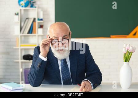 Insegnante anziano che tiene una lezione. Insegnante senior che aiuta gli studenti. Insegnante senior all'università. Insegnante senior che scrive sulla lavagna. Foto Stock