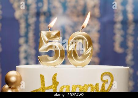 Il numero "50" di candele accese su una torta di compleanno durante una festa. Simboleggia un'epoca di pietra miliare con un'illuminazione calda e un'atmosfera dolce. Foto Stock