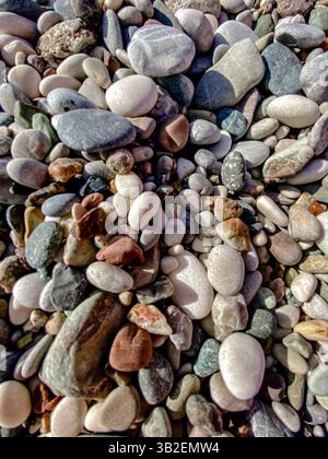 Ciottoli e pietre colorati e lisci sulla spiaggia in primo piano che mostrano una consistenza e varietà naturali. Foto Stock