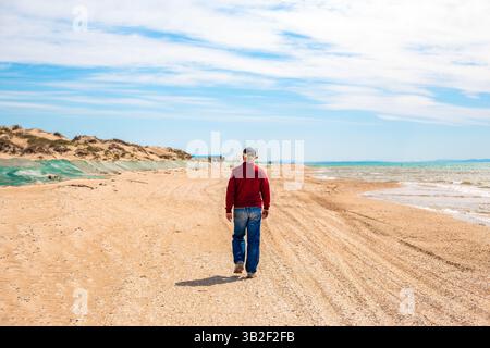 Fuoriuscita di olio combustibile. Un uomo cammina lungo una spiaggia sabbiosa con una duna di sabbia coperta da una rete protettiva di olio combustibile gettata sulla riva da un'onda. Foto Stock