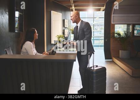 Addetto alla reception, personale e addetto al check-in per la sistemazione durante un viaggio di lavoro. Donna, dipendente e cliente o cliente maschio con un sorriso in aiuto Foto Stock