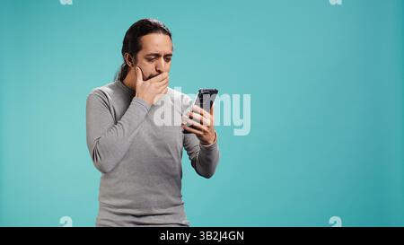 Uomo che ha un telefono cellulare, sta navigando sul sito di scommesse, festeggia dopo aver vinto soldi, isolato sullo sfondo dello studio. Persona allegra che si sente felice mentre scorri sullo smartphone o sulla fotocamera B. Foto Stock