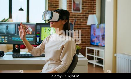 La creatrice di video donna asiatica utilizza un visore per la realtà virtuale alla sua scrivania, strumenti tecnologici moderni per la sua occupazione creativa. Artista femminile che modifica e mixa video clip per progetti cinematografici. Telecamera A.. Foto Stock