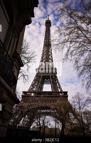 Torre Eiffel incorniciata da edifici e alberi parigini sotto un luminoso cielo invernale. Scatto con orientamento verticale. Foto Stock