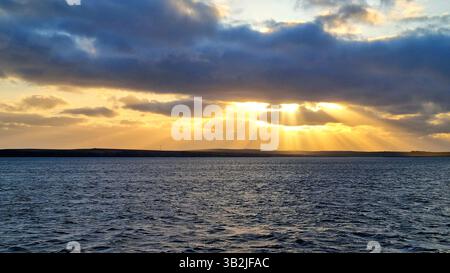 I raggi dorati del sole che tramonta penetrano nell'oscurità delle nuvole e illuminano le acque scure dell'Oceano Atlantico Foto Stock