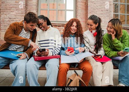 Un vivace gruppo di studenti impegnati in conversazione, condividendo i loro dispositivi mobili e le loro idee, mostrando cameratismo e amicizia tra i giovani studenti Foto Stock