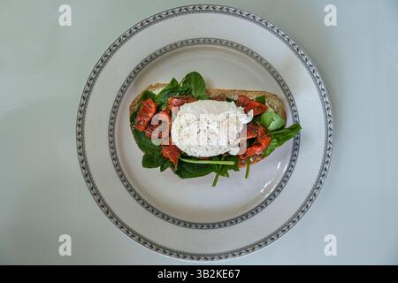 una deliziosa colazione con uova in camicia su una fetta di ciabatta con spinaci e pezzetti di pesce rosso salato Foto Stock