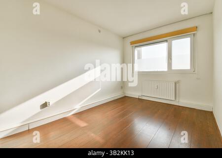 Una camera minimalista con pavimenti in legno duro e luce soffusa del sole che scorre attraverso una finestra, creando un'atmosfera serena e un'estetica moderna. Foto Stock