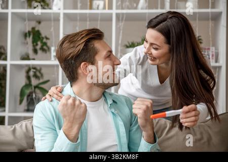 Una coppia entusiasta e gioiosa che celebra insieme i risultati positivi del test di gravidanza Foto Stock