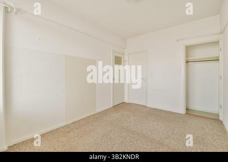 Una camera spaziosa e ordinata caratterizzata da pareti di colore chiaro, pavimento in moquette e un semplice armadio. Ideale per l'ispirazione di interior design o per inserzioni immobiliari. Foto Stock
