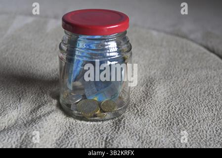 Banconote e monete in un vaso di vetro. Foto Stock