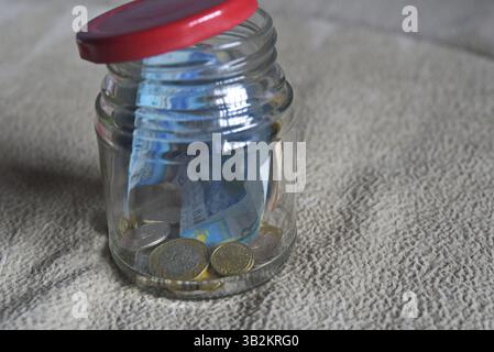 Banconote e monete in un vaso di vetro. Foto Stock