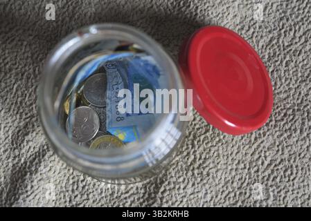 Banconote e monete in un vaso di vetro. Foto Stock