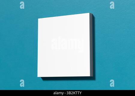 Composizione minimalista caratterizzata da una tela quadrata bianca bianca su una vivace parete blu acqua, ideale per mostrare opere d'arte o disegni. Rendering 3D. Foto Stock