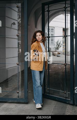 Milionario che sorride nella vita cittadina con il telefono in mano. Potenziamento digitale, stile casual e routine tecnologiche... Foto Stock