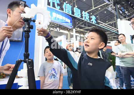 Un ragazzo interagisce con un braccio robot. Hefei, Cina. 26 aprile 2025. La terza fiera cinese (Anhui) per la trasformazione dei risultati dell'innovazione scientifica e tecnologica prende il via a Hefei, capitale della provincia di Anhui nella Cina orientale, il 26 aprile 2025. Credito: Han Suyuan/China News Service/Alamy Live News Foto Stock