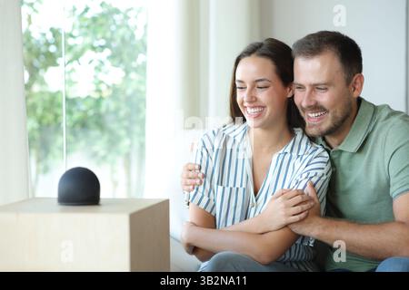 Coppia felice che si diverte a guardare il nuovo altoparlante intelligente seduto sul divano di casa Foto Stock