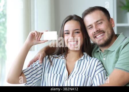 Coppia felice che mostra una carta bianca seduta su un divano a casa Foto Stock