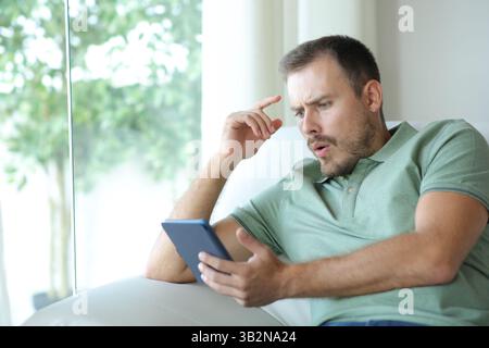 Un uomo sospeso che legge un eBook dopo un colpo di scena seduto su un divano a casa Foto Stock