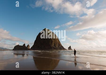 Un uomo cammina lungo la costa dell'Oregon vicino a Haystack Rock Foto Stock