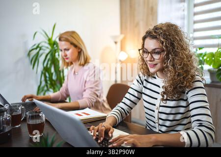 Due colleghi donne a una scrivania che lavorano su un computer portatile Foto Stock