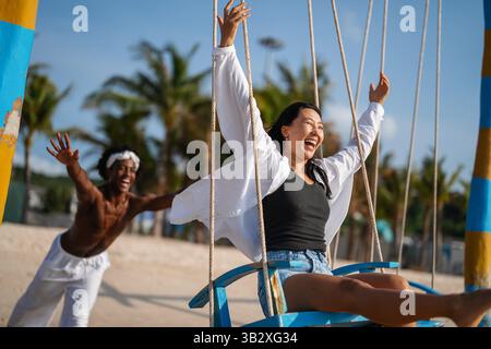 Coppia interrazziale godendo la libertà dell'estate, ridendo e giocando su una spiaggia tropicale Foto Stock