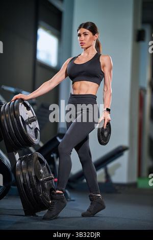 In una palestra ben attrezzata, la donna esegue l'allenamento di forza, sollevando pesi. Indossa gli outfit sportivi e dimostra concentrazione durante l'allenamento Foto Stock