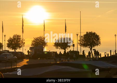 Sirmione, Italia - 01.2022: Tramonto dorato sul lungomare con sagome di persone e bandiere, lago di Garda Foto Stock