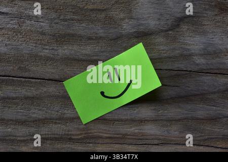 Faccia Smiley su note adesive gialle su sfondo testurizzato in legno. Il pennarello nero disegna la faccia sorridente su carta per appunti. Foto Stock