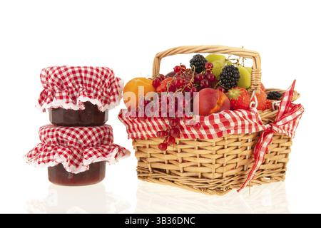 Cesto in Vimini con Frutta estiva fresca e pentole jam isolate su sfondo bianco Foto Stock
