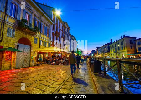MILANO, ITALIA - 8 APRILE 2022: Al calare della sera, gente del posto e turisti condividono la passeggiata lungo il canale del Naviglio, l'8 aprile a Milano, Italia Foto Stock