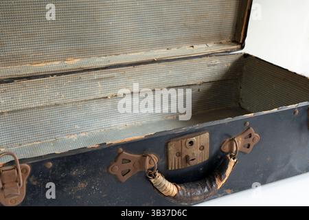 La vecchia valigia in metallo arrugginito è vuota con coperchio aperto e mostra l'interno in cartone. L'antica maniglia per bagagli è in pelle, corda e legno. Ideale per la visualizzazione. Foto Stock