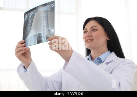 Medico sorridente che esamina la scansione RM del collo in clinica, vista ad angolo basso Foto Stock