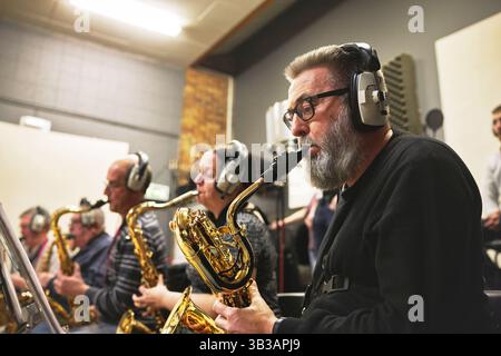 Musica, band e sassofono con persone in uno studio di registrazione, leggendo note musicali per una performance. Concerto, jazz e un gruppo maturo che suona un Foto Stock