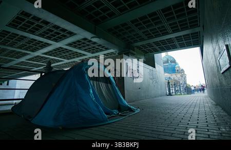 Tenda di un senzatetto sotto un ponte a Berlin-Mitte, con la cattedrale di Berlino visibile sullo sfondo attraverso il fiume, germania povertà. Foto Stock