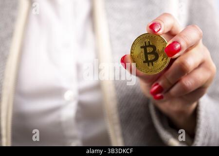 Moneta criptovaluta virtuale Bitcoin moneta d'oro nella mano sinistra di una donna con smalto rosso. Il futuro del denaro Foto Stock