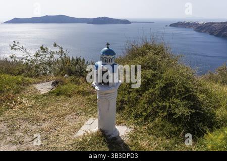 Piccola chiesa come pietra commemorativa, dietro l'isola di Thirassia e Oia, Santorini, Grecia, Europa Foto Stock