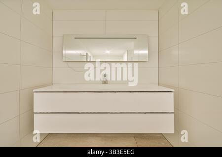 Dotato di un elegante lavandino bianco e di un grande specchio, questo bagno incarna un'eleganza minimalista con linee pulite e un'atmosfera luminosa. Foto Stock