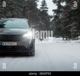 Angolo anteriore della Peugeot 5008 nella foresta invernale. Crossover grigio scuro parcheggiato su un lato innevato di una strada nella pineta. Foto Stock