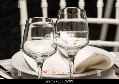 Due bicchieri da vino vuoti su un tavolo decorato, preparati per una festa di compleanno o un'elegante festa con luci soffuse. Foto Stock