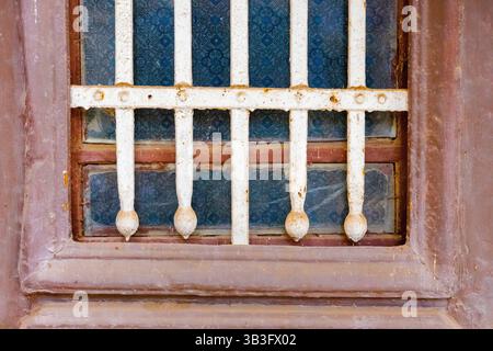 Primo piano delle barre di ferro arrugginite sulla finestra Vintage con vetro a fantasia blu in Egitto Foto Stock