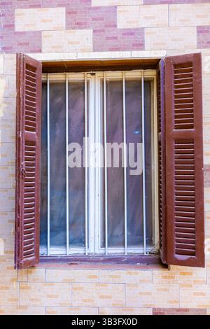 Vecchia finestra con tende in legno aperte e barre di sicurezza in metallo in Egitto Foto Stock