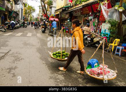 Una donna porta frutta in vendita ad Hanoi, Vietnam Foto Stock